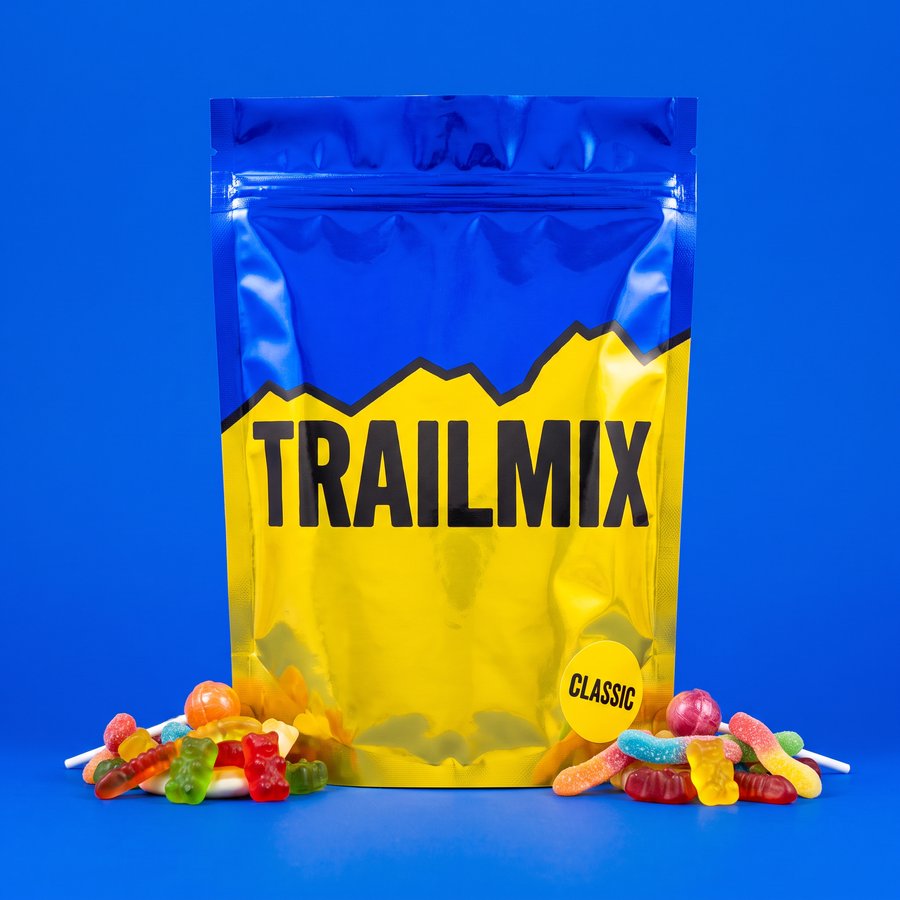 A blue and yellow Trailmix Classic pouch with gummy sweets spilling out